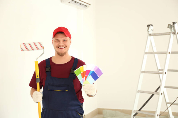Male painter in uniform with roller brush and color palette samples indoors - Photo, Image