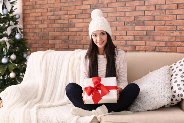 Beautiful young woman in hat with gift box at home. Christmas celebration - Foto, Bild