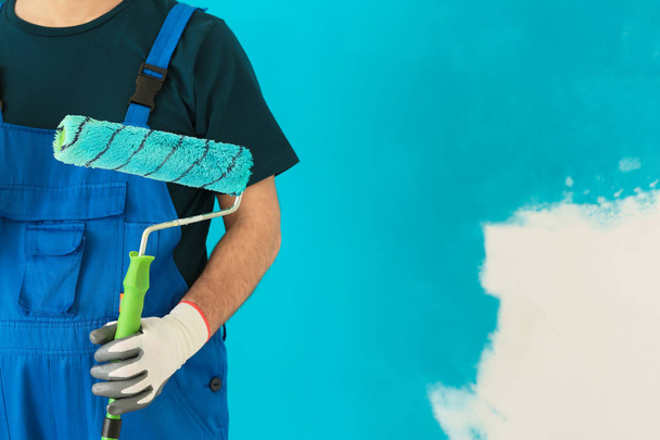 Male painter in uniform with roller brush  on color background - Foto, Imagen