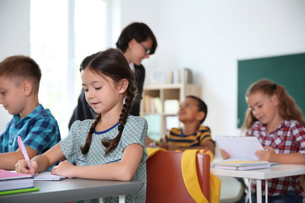 Adorable little children sitting at desks in classroom. Elementary school - Zdjęcie, obraz