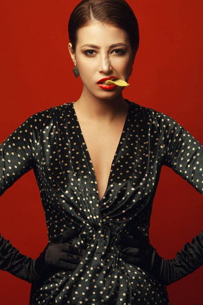 Unhealthy eating. Junk food obsession concept. Portrait of fashionable luxurious young woman holding fried potato chips in mouth, posing over red background. Studio shot - Fotografie, Obrázek