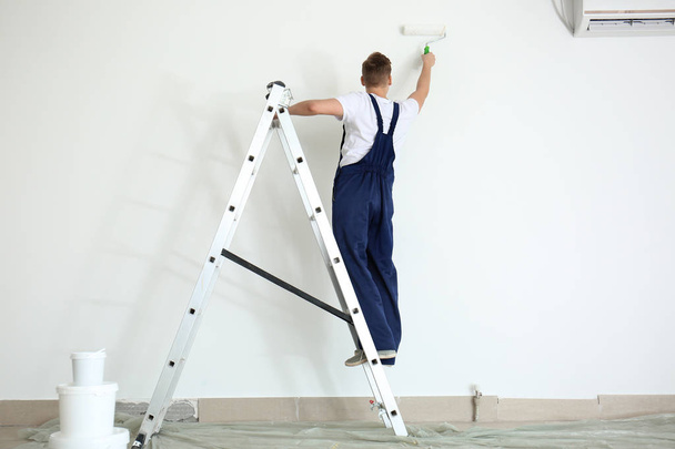 Peintre masculin utilisant un rouleau pour remettre à neuf la couleur du mur à l'intérieur
 - Photo, image
