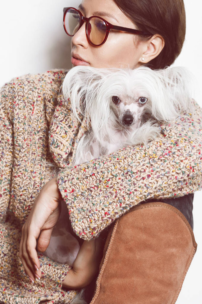 Best girlfriends concept. Young gorgeous lady with natural make-up wearing trendy clothes, eyeglasses holding small dog over white background. Street fashion style. Indoor shot - Foto, afbeelding
