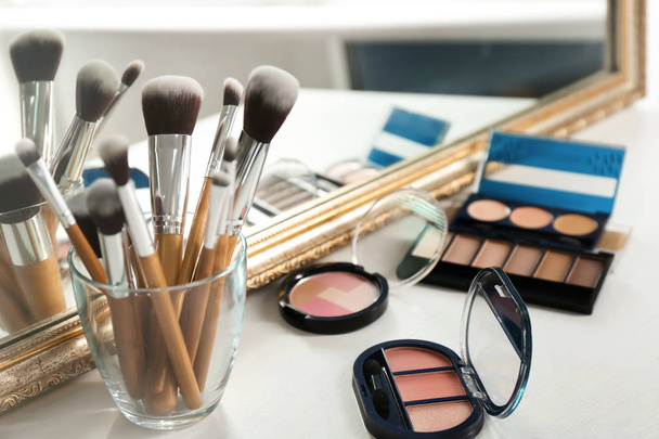 Set of makeup brushes with decorative cosmetics on table near mirror - Photo, Image