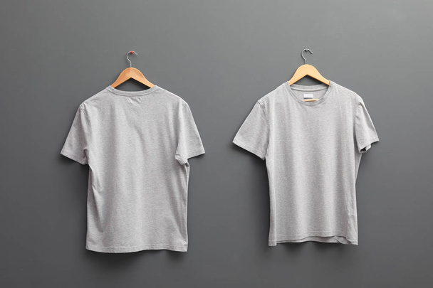 Hangers with blank t-shirts on grey background. Mockup for design - Fotó, kép