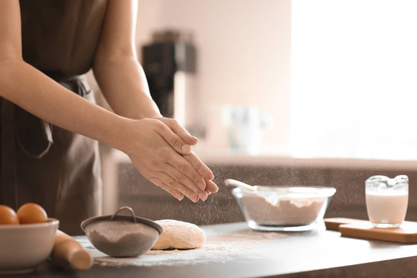 Baker sprinkling flour on dough at table - Foto, imagen