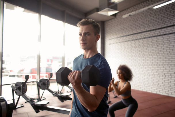 Hombre atlético haciendo ejercicio con la mancuerna en el gimnasio moderno
 - Foto, imagen