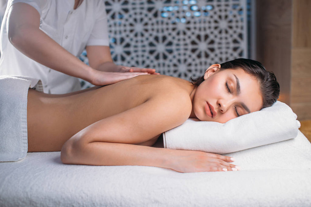 Beautiful young woman lying on bed while masseur massaging her back - Valokuva, kuva