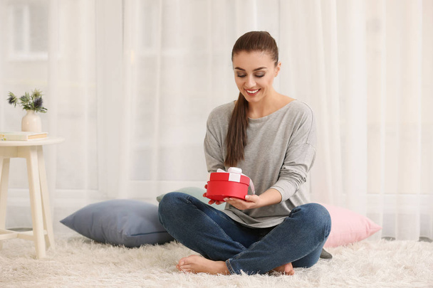Beautiful young woman with gift box at home - Foto, Bild