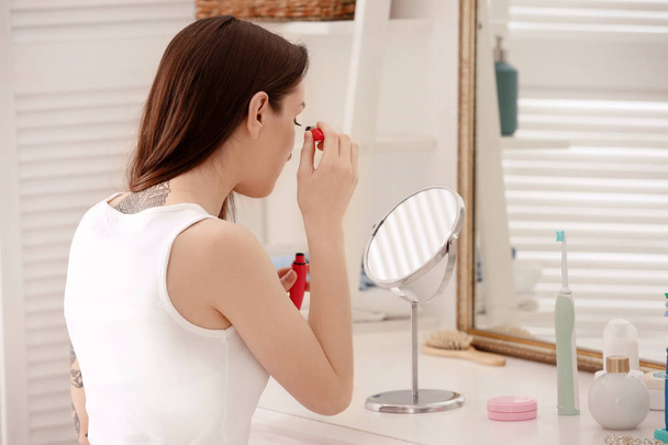 Nuori kaunis nainen soveltamalla meikki lähellä peili sisätiloissa. Huomenta rutiini
 - Valokuva, kuva