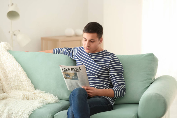 Handsome man reading newspaper on sofa at home - Фото, зображення