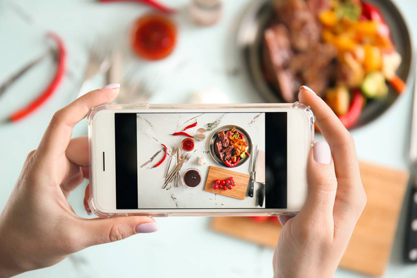 Woman taking photo of barbecue sauce and grilled meat with mobile phone, top view - 写真・画像