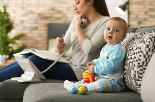 Cute little baby sitting on sofa while mother working at home - Photo, Image