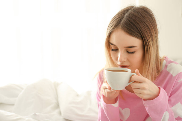 Huomenta kaunis nuori nainen juo kuumaa kahvia makuuhuoneessa
 - Valokuva, kuva
