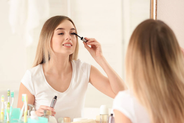 Beautiful young woman applying makeup in morning - Foto, afbeelding