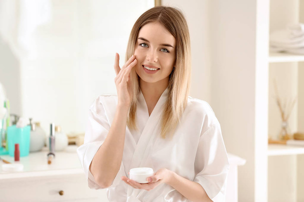 Beautiful young woman applying cream in morning - Zdjęcie, obraz