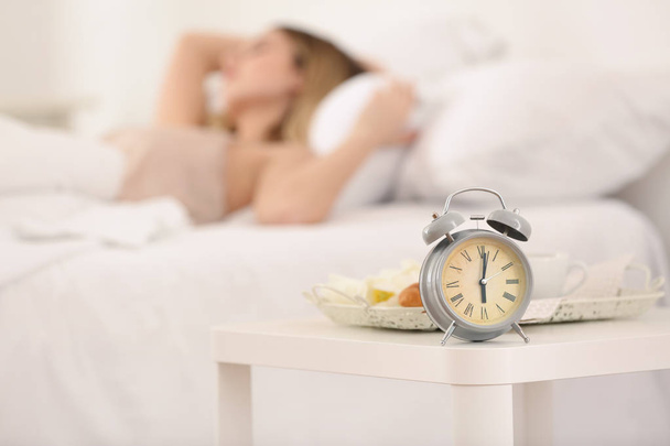 Alarm clock on table in bedroom of beautiful young woman. Morning time - Foto, afbeelding