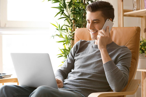 Młody freelancer rozmowy na telefon podczas korzystania z laptopa w domu - Zdjęcie, obraz