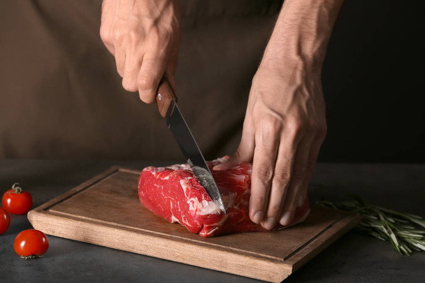 Man cutting fresh raw meat on wooden board - Photo, Image