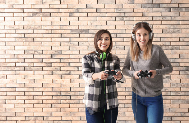 Jovens mulheres com gamepads no fundo da parede de tijolo
 - Foto, Imagem