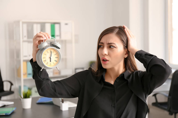 Troubled woman with alarm clock in office. Time management concept - Photo, Image