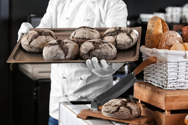 Мужчина пекарь держит поднос со свежим хлебом в магазине
 - Фото, изображение