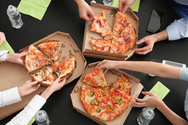 Молодые люди едят пиццу за столом в офисе, вид сверху
 - Фото, изображение