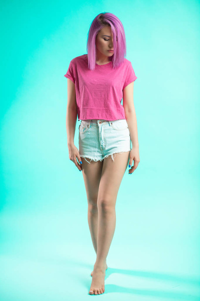 Slim fit sporty active woman in denim shorts looking at camera isolated on blue background - Foto, Imagem