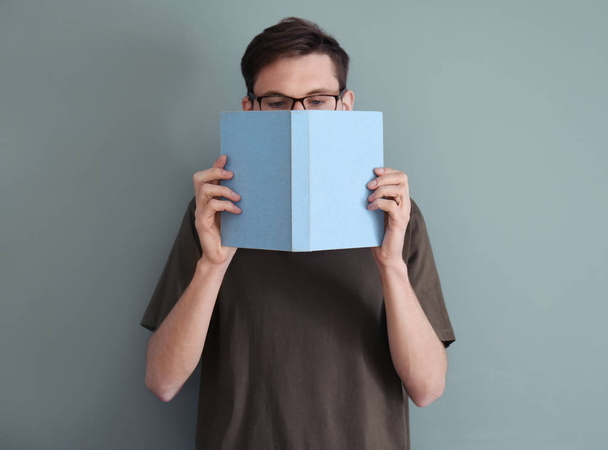 Young man reading book on color background - Fotó, kép