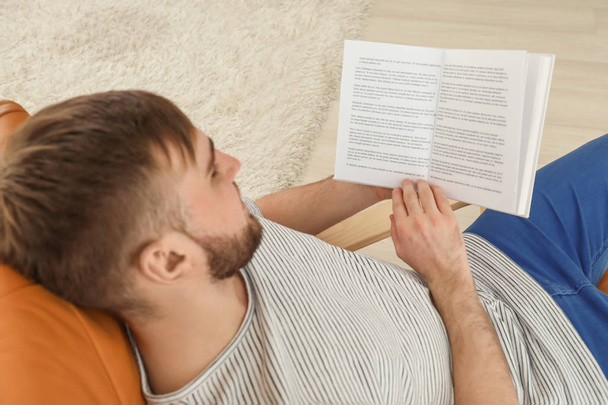 молодий чоловік читає книгу вдома
 - Фото, зображення