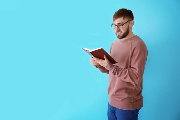 Νεαρός άνδρας διαβάζει το βιβλίο στο φόντο χρώμα - Φωτογραφία, εικόνα