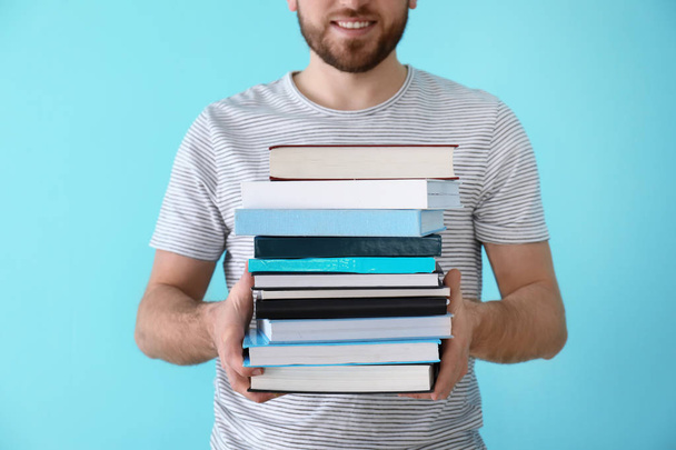 Young man with stack of books on color background - Photo, Image