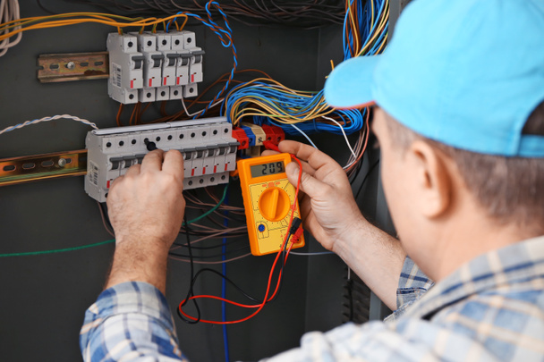 Mature electrician measuring voltage in distribution board - Photo, image