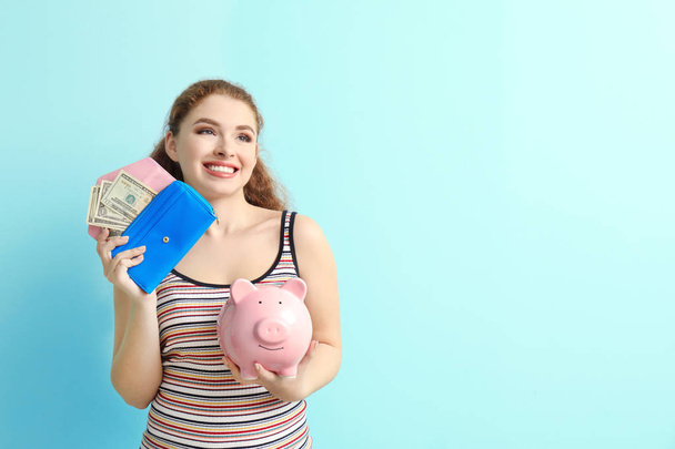 Young woman holding piggy bank and wallet with dollar banknotes on color background. Money savings concept - Photo, Image