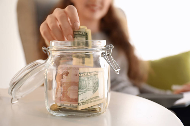 Jeune femme mettant billet de dollar dans un bocal en verre à l'intérieur, gros plan. Concept d'épargne monétaire
 - Photo, image