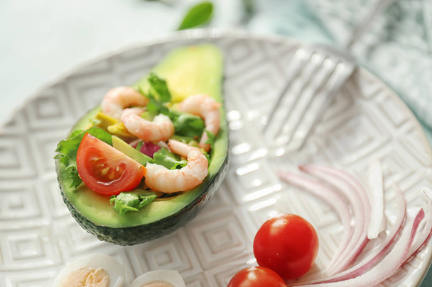Вкусный салат из креветок в лодке авокадо на тарелке, крупный план
 - Фото, изображение
