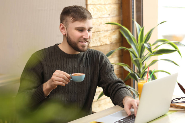 Young freelancer drinking coffee while working on laptop in cafe - Фото, зображення