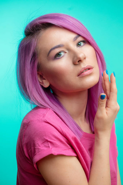 Attractive girl with pink hair, dressed in casual pink cloth on blue background. - Fotó, kép