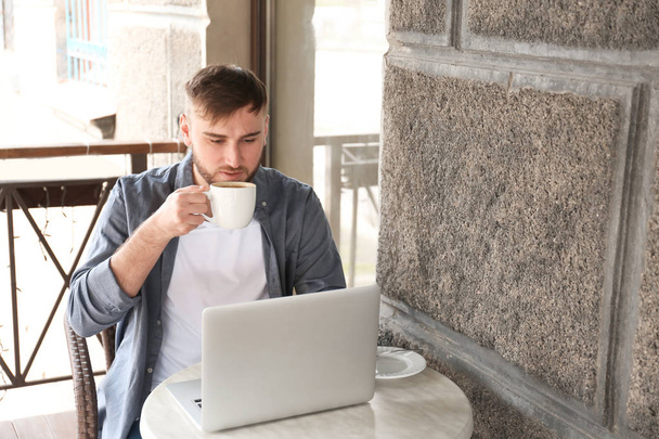Молодий фрілансер п'є каву під час роботи на ноутбуці в кафе
 - Фото, зображення