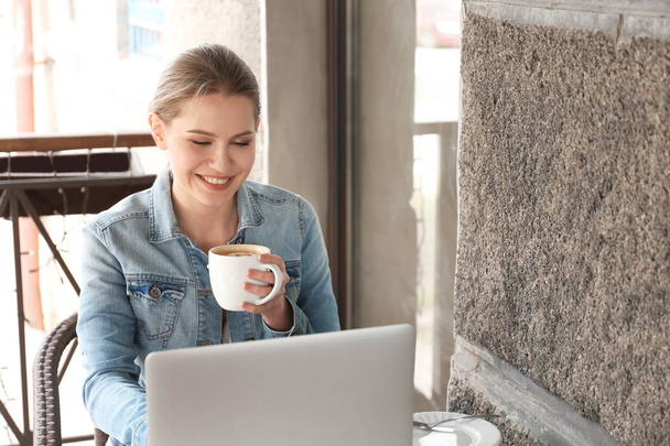 Joven freelancer bebiendo café mientras trabaja en la computadora portátil en la cafetería
 - Foto, imagen