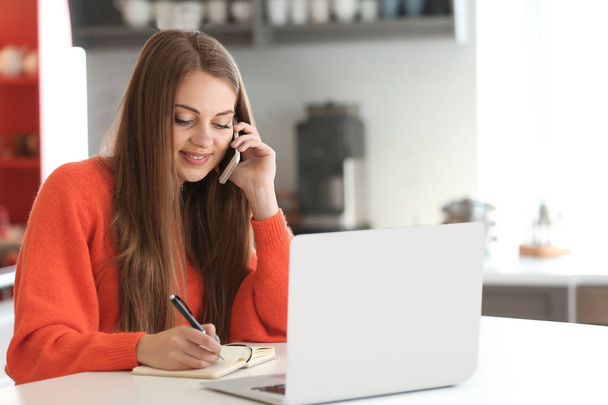Female freelancer talking by phone while working at home - Photo, Image