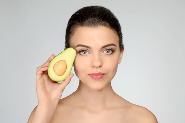 Beautiful young woman with avocado on light background - Photo, image