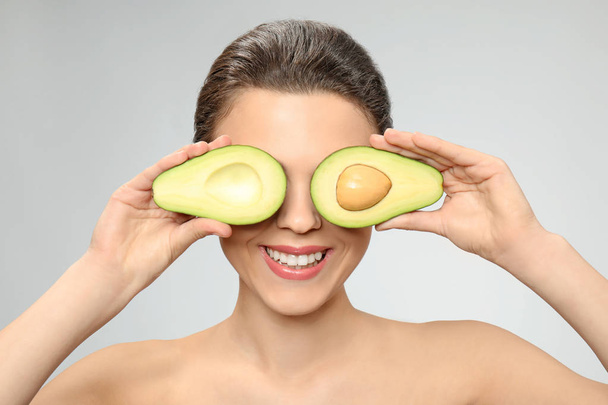 Funny young woman with avocado on light background - Photo, Image