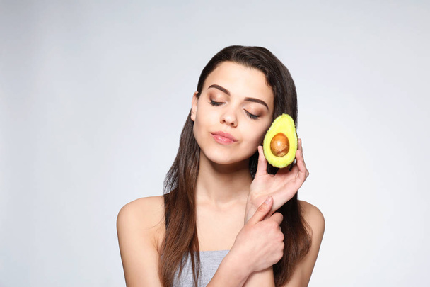 Beautiful young woman with avocado on light background - Photo, Image