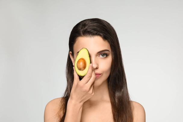 Beautiful young woman with avocado on light background - Fotó, kép