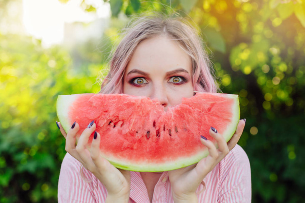 Beautiful young woman with pink hair enjoying sweet juicy watermelon - Foto, imagen