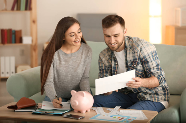 Gelukkige paar met betalen rekeningen, rekenmachine en geld tellen kosten binnenshuis. Geld besparing concept - Foto, afbeelding