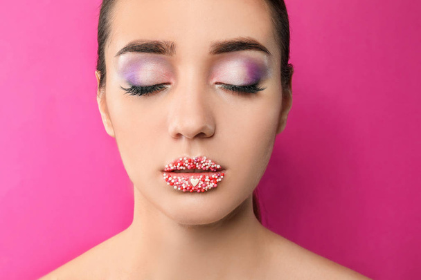 Mooie jonge vrouw met creatieve make-up op kleur achtergrond - Foto, afbeelding