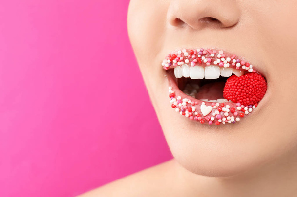 Beautiful young woman with creative makeup and candy in mouth on color background, closeup - Foto, Imagen