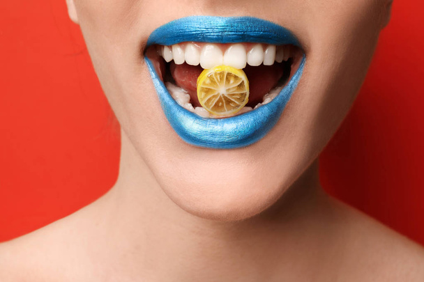 Beautiful young woman with creative makeup and candy in mouth on color background, closeup - Photo, Image